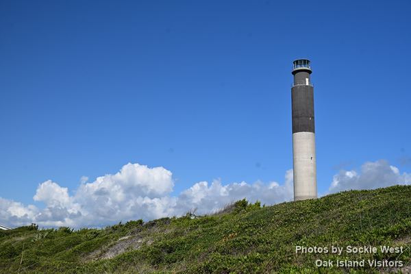 Oak Island Lighthouse above the dune shrubs under a blue sky, Caswell Beach