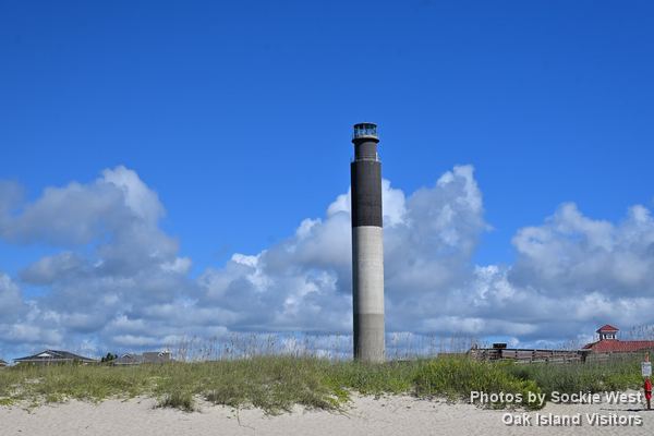 Oak Island Lighthouse seen across the beach and dune grass with summer clouds